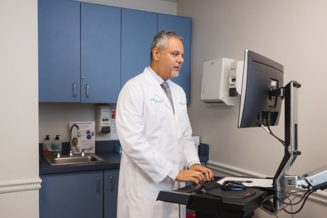Doctor in a white lab coat using a computer in a medical office with blue cabinets in Atlanta, GA
