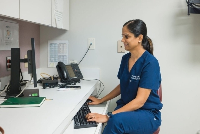 Doctor in navy scrubs working on a desktop computer at an office desk in Atlanta, GA

