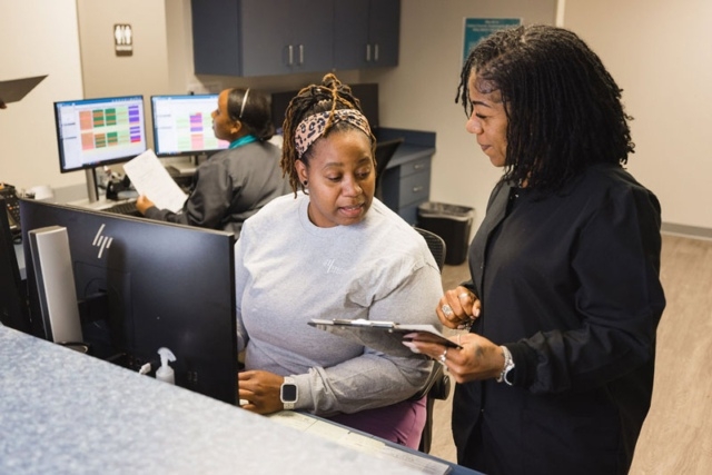 office-team-staff-discussing Two People at a Computer Desk in the GI Specialists of Georgia's Office, with a Clipboard